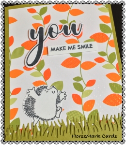 Hedgehog dancing above grass on leaves background paper, ‘You make me Smile’ message created by HorseMark Cards